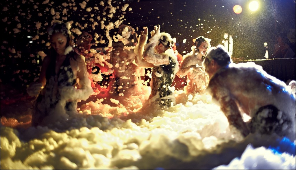 A group of young adults dancing in foam at night