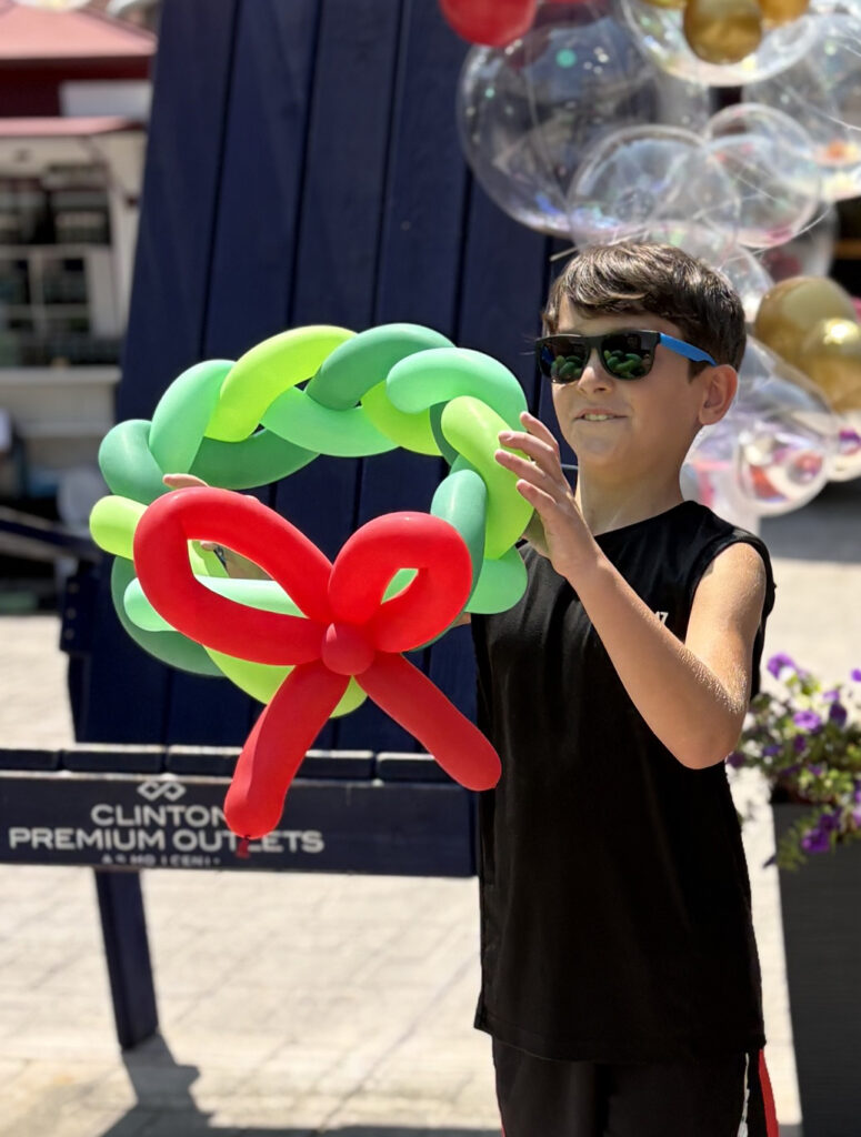 A boy in a tshirt and sun glasses outside holding a Christmas balloon