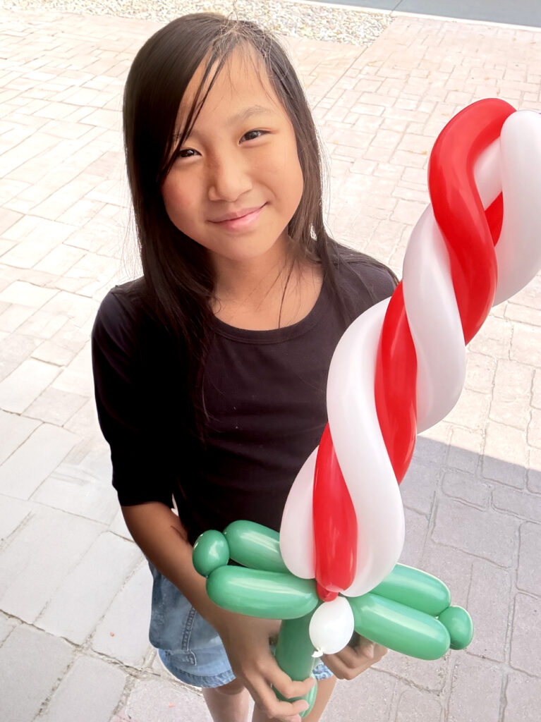 A girl holding a candy cane sword balloon at a Christmas in July event